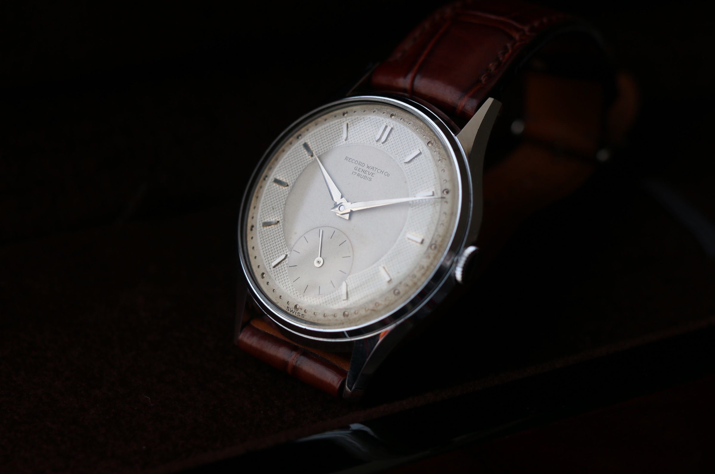 Record Genève wristwatch photographed at an oblique angle showing the stepped bezel and faceted lugs