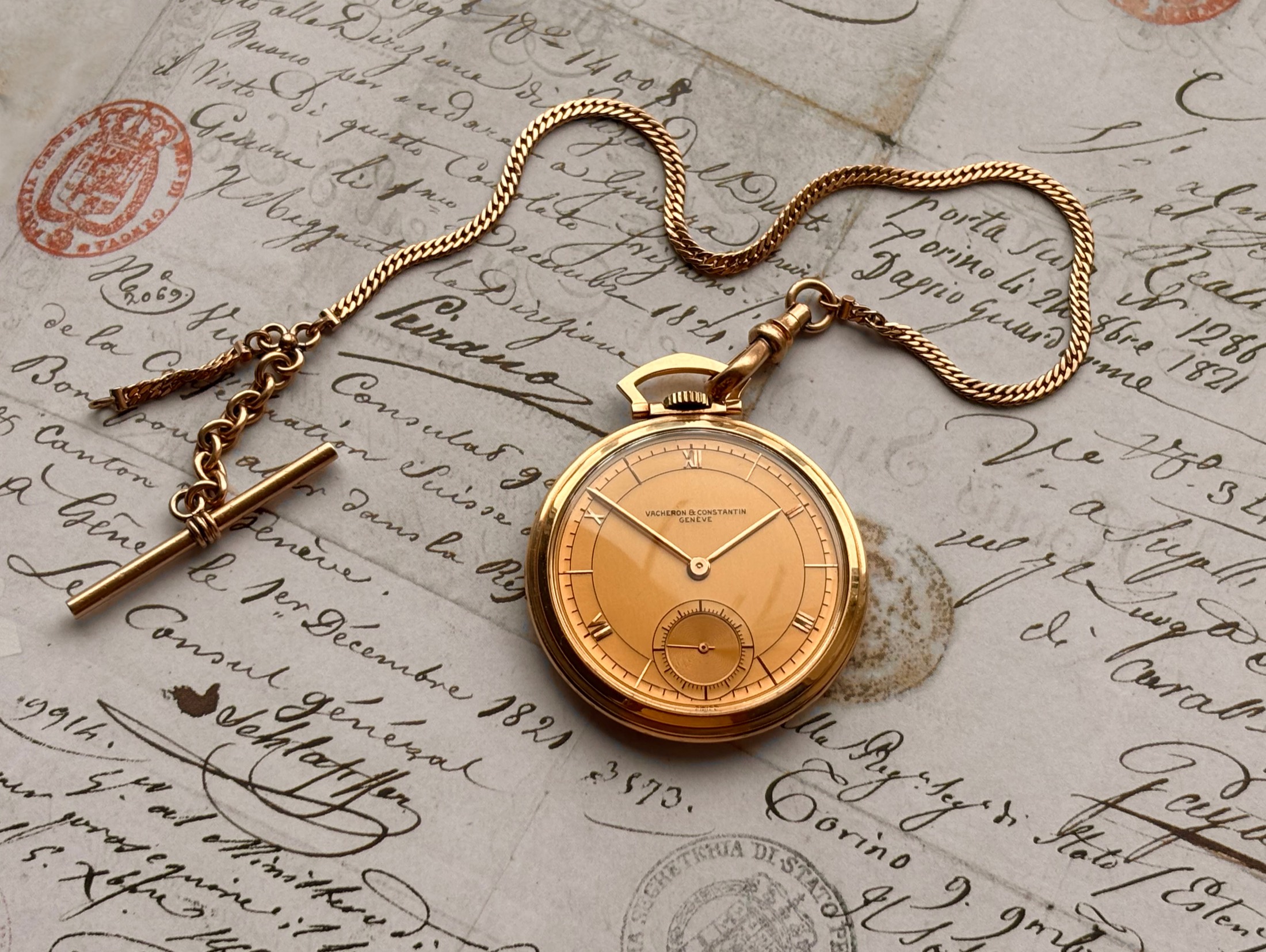 This Vacheron & Constantin pocket watch and gold chain resting on a wooden desk